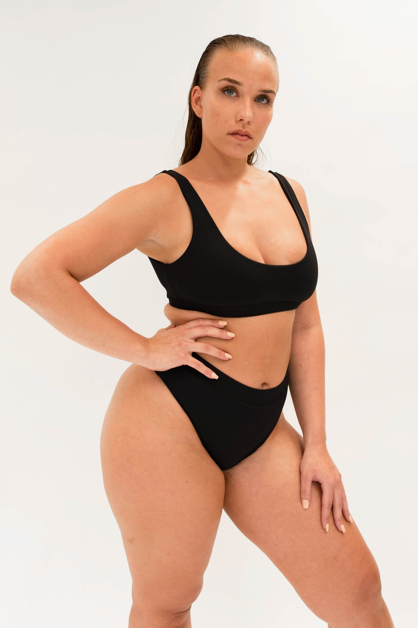 model with black sustainable high cut bikini bottom and sporty top 